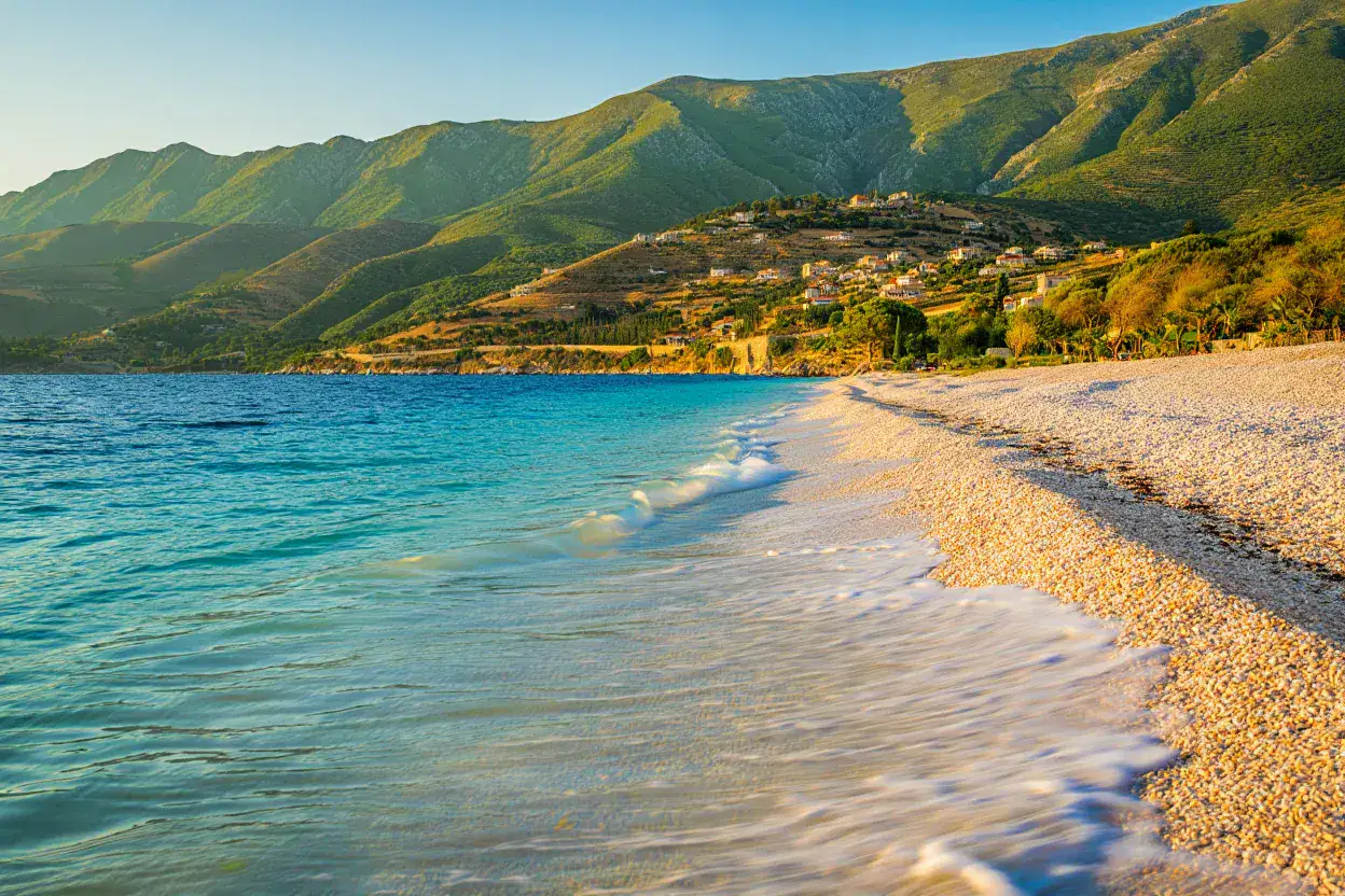 Côte turquoise de la Riviera albanaise près de Saranda, plage de galets blancs et montagnes vertes au coucher du soleil