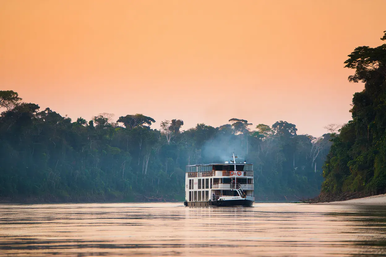 Bateau de croisière fluviale naviguant sur l'Amazone au coucher du soleil entre deux rives de forêt tropicale, aucune présence humaine