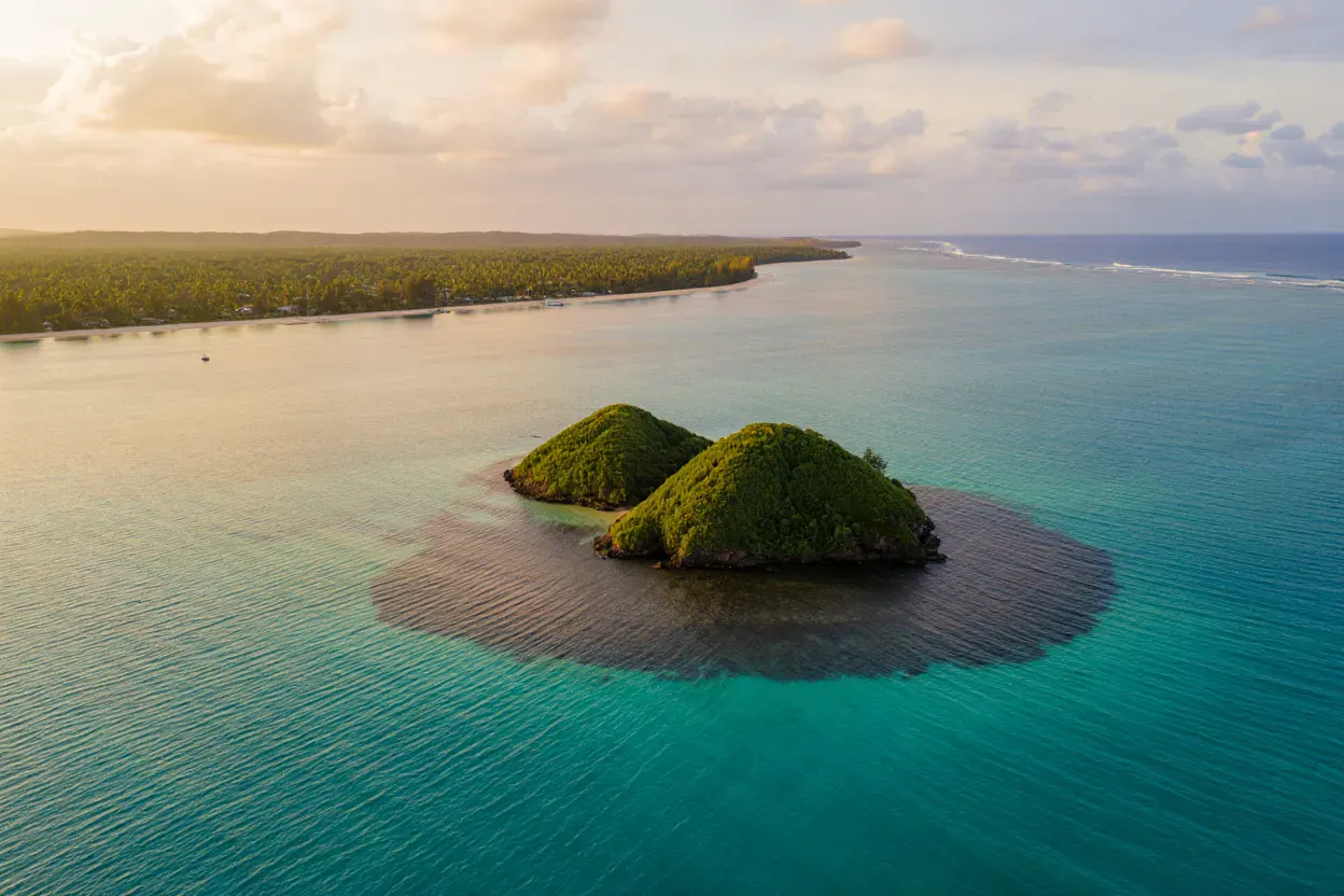 Petite île tropicale aux deux collines boisées dans une mer turquoise au large d'une plage bordée de palmiers du Queensland, lumière dorée, aucune présence humaine