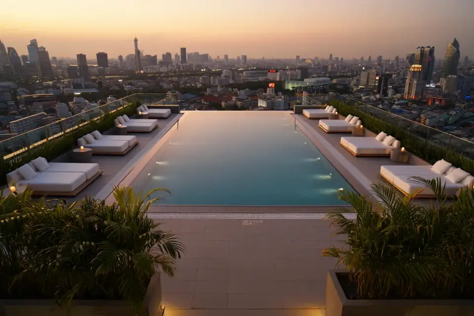 Piscine sur le toit d'un hôtel au coucher du soleil, transats vides et vue sur une grande ville d'Asie, ambiance de luxe accessible
