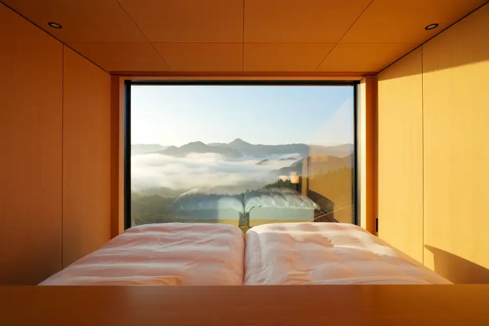 Chambre d'hôtel de luxe silencieuse, lumière dorée, literie blanche, fenêtre épaisse donnant sur un paysage calme
