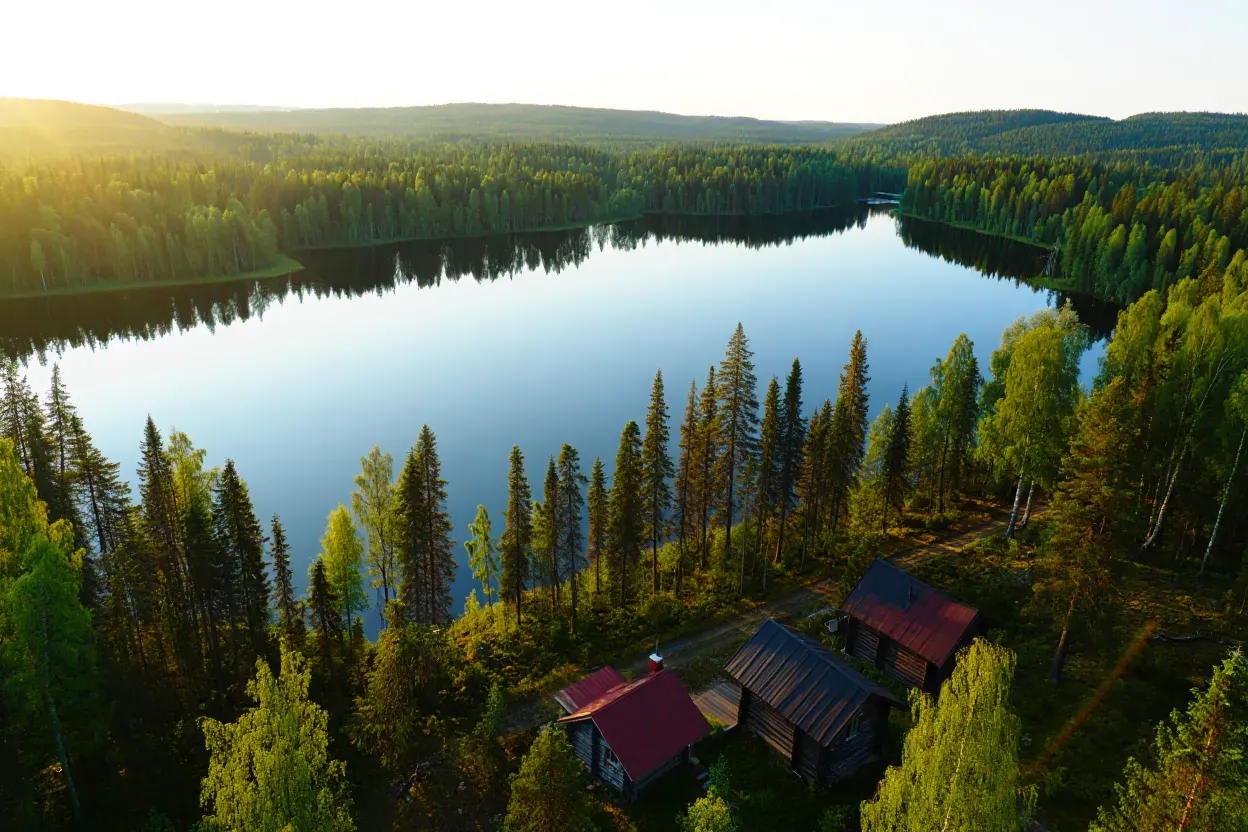 Lac et chalets en bois de Laponie finlandaise sous la lumière dorée du soleil de minuit, forêt de conifères en arrière-plan