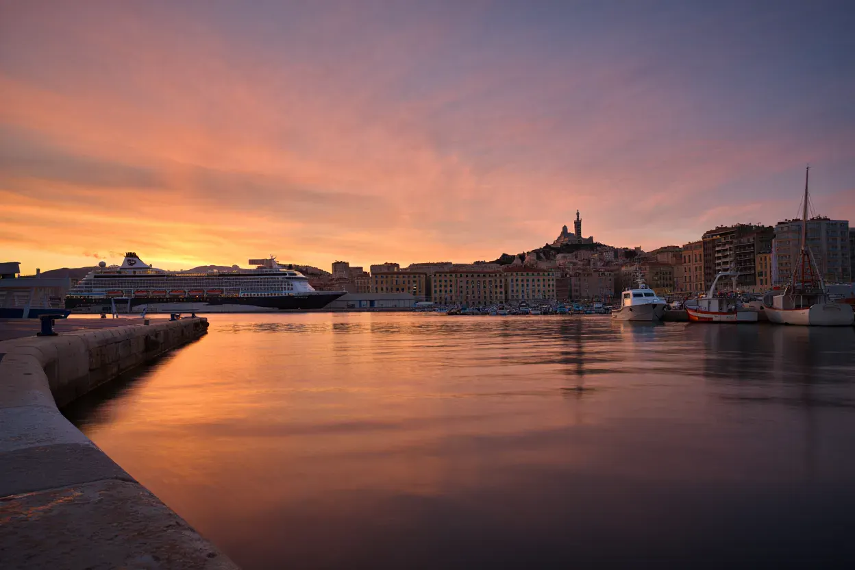 Vue du Vieux-Port de Marseille au coucher du soleil avec un paquebot de croisière amarré et la basilique Notre-Dame de la Garde en arrière-plan