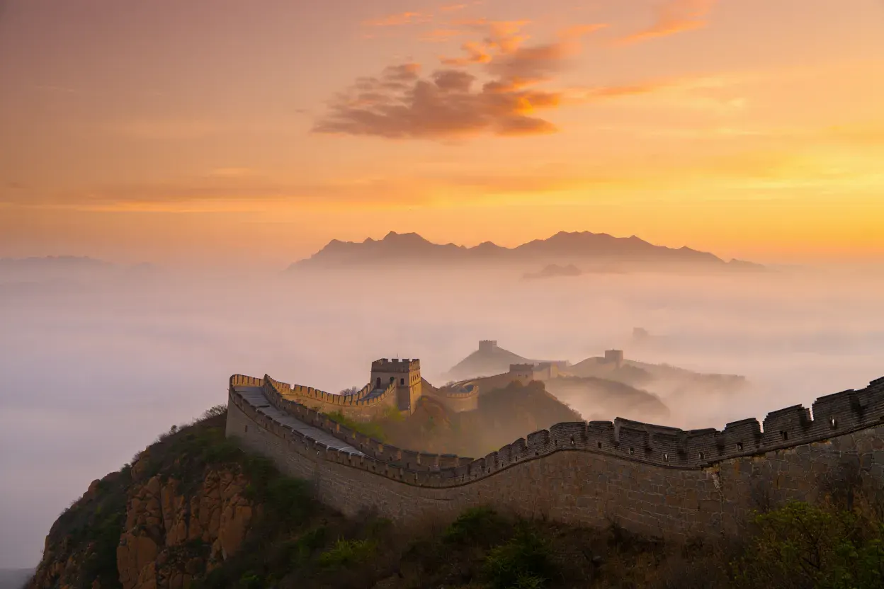 La Grande Muraille de Chine serpentant sur des crêtes montagneuses dans la brume dorée du soir, sans personne
