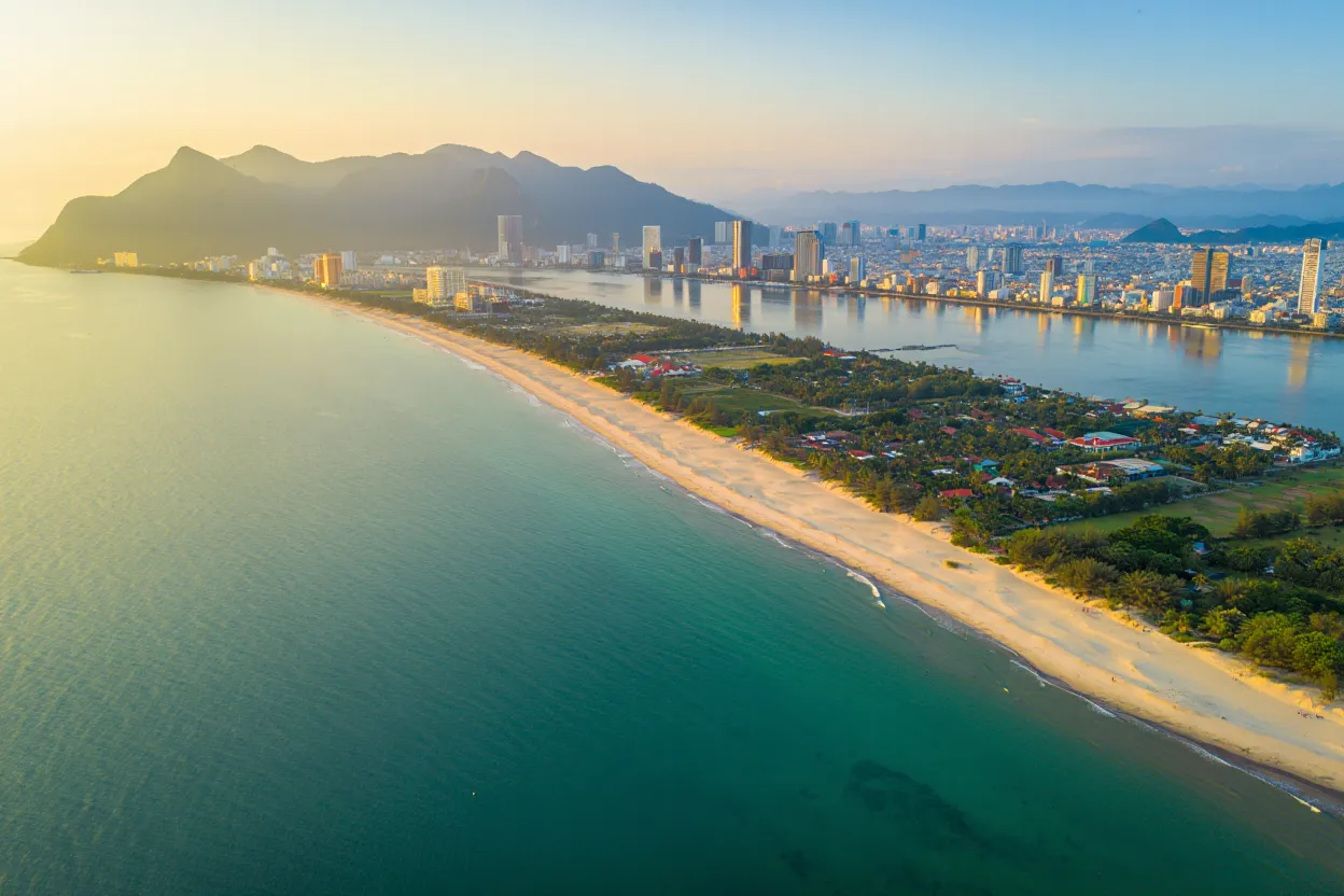 Longue plage de sable blanc de Da Nang au bord de la mer de Chine méridionale, avec les Montagnes de Marbre et la chaîne annamite en arrière-plan au coucher du soleil